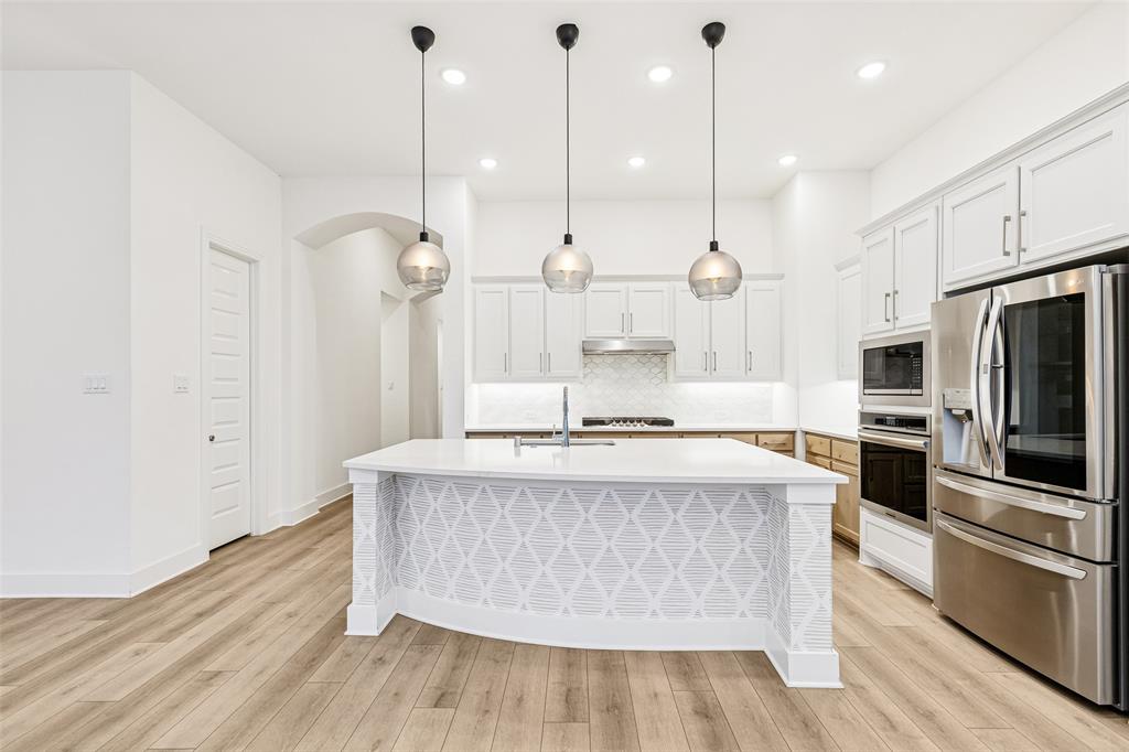 1144 Saddle Ridge Drive Aubrey, TX 76227 - Photo 6 of 34 a large kitchen with stainless steel appliances a large counter top a sink a refrigerator and a wooden floor