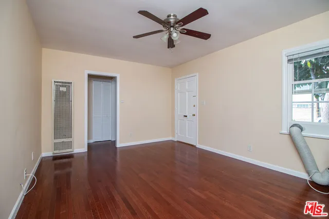 an empty room with wooden floor fan and windows