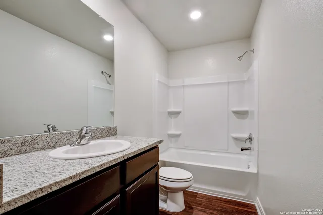 a bathroom with a granite countertop sink a toilet a mirror a bathtub and shower