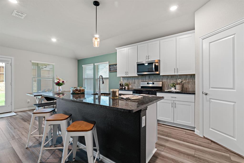 3112 Kingsgarden Road Denton, TX 76207 - Photo 14 of 38 Modern kitchen featuring a spacious dark-toned island with a built-in sink and faucet, white cabinetry, integrated microwave, and wood-finish flooring