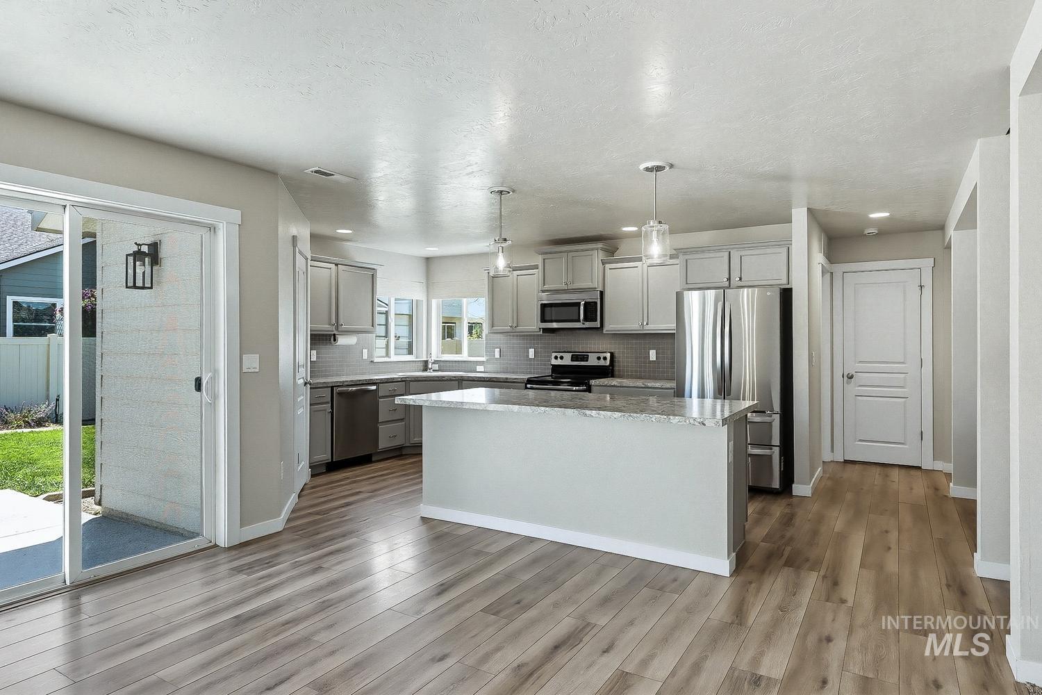 846 North Hidden View Way Star, ID 83669 - Photo 9 of 49 Open-concept kitchen featuring light-toned cabinetry, stainless steel appliances, a center island with a stone-finish countertop, and wood-finish flooring