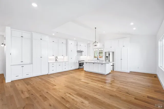 a large white kitchen with kitchen island a sink stainless steel appliances and cabinets