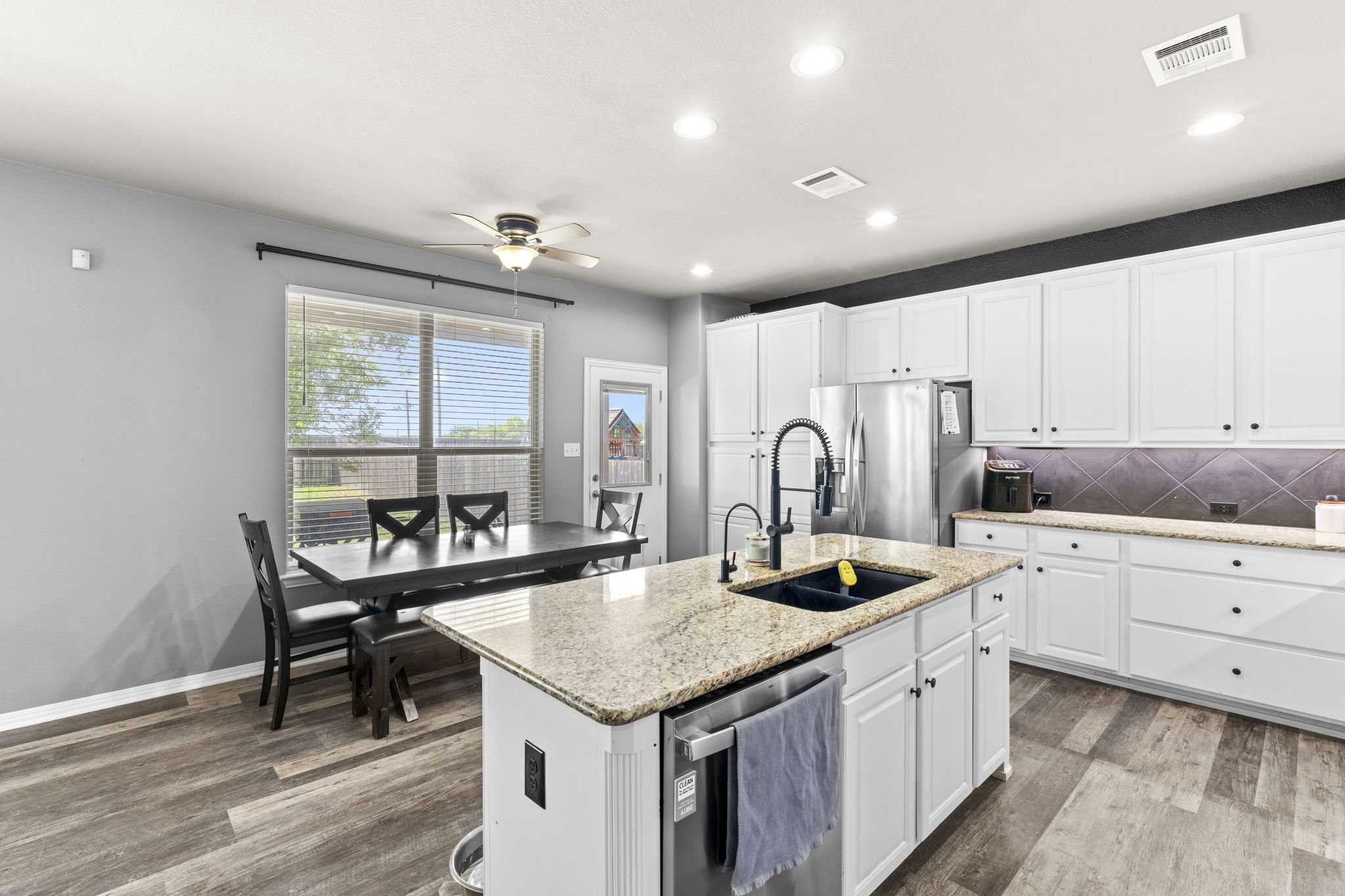 227 Sandstone Trail Buda, TX 78610 - Photo 6 of 33 Kitchen featuring white cabinetry, granite countertops, a central island with an undermount sink, stainless steel appliances, and wood-finish flooring