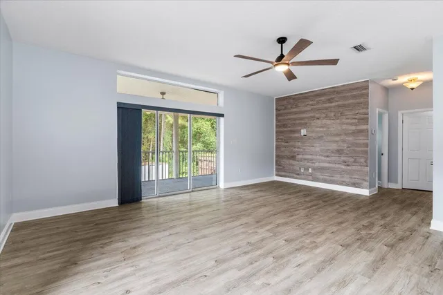 an empty room with wooden floor kitchen view and a window