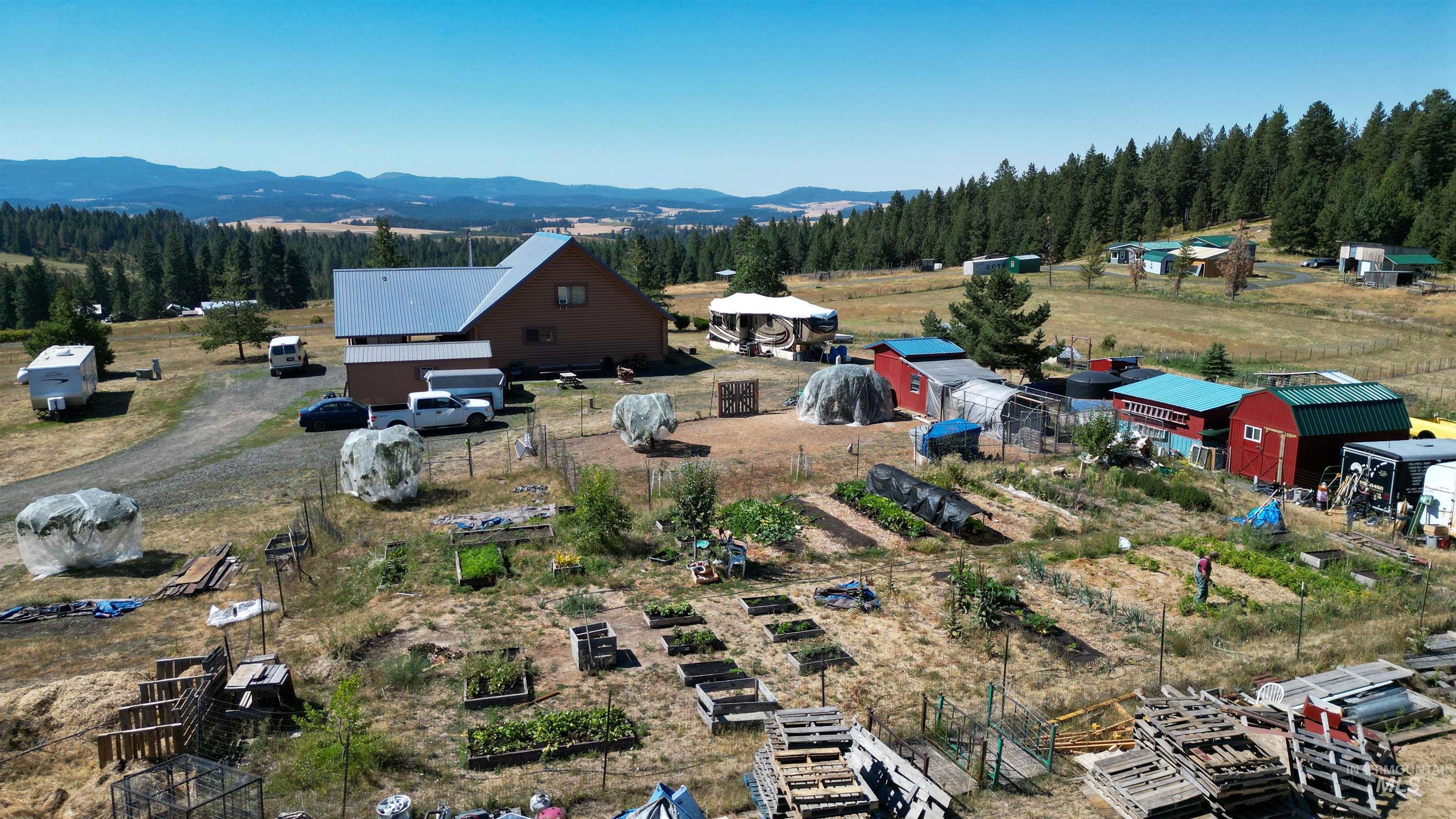 1321 Gold Hill Road Princeton, ID 83857 - Photo 28 of 29 Expansive rural property featuring a main residence with a metal roof, multiple outbuildings, raised garden beds, and mature trees