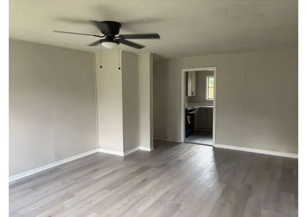 a view of an empty room with wooden floor and a ceiling fan