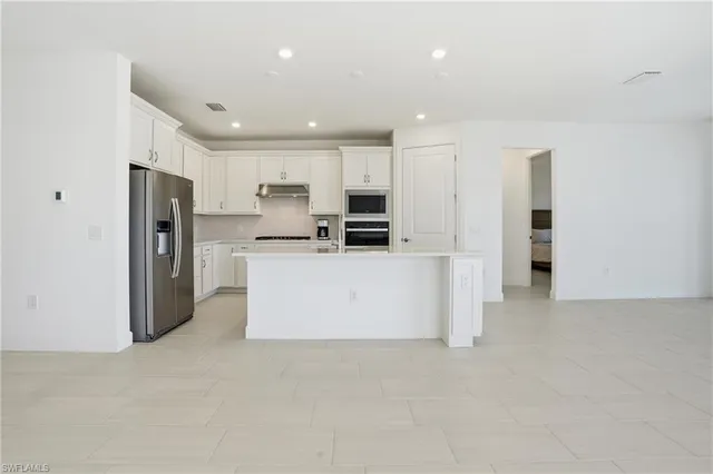 a large kitchen with stainless steel appliances refrigerator a microwave and white cabinets