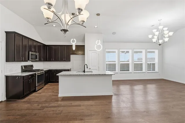 a kitchen with stainless steel appliances granite countertop a sink dishwasher a stove and a dining table with wooden floor