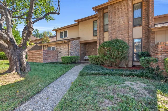 a view of a brick house with a yard large tree and a large window
