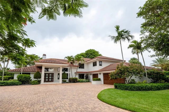 a view of a white house in a big yard with large trees and plants