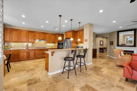 a dining hall with stainless steel appliances kitchen island granite countertop a refrigerator a stove a sink with a dining table and chairs