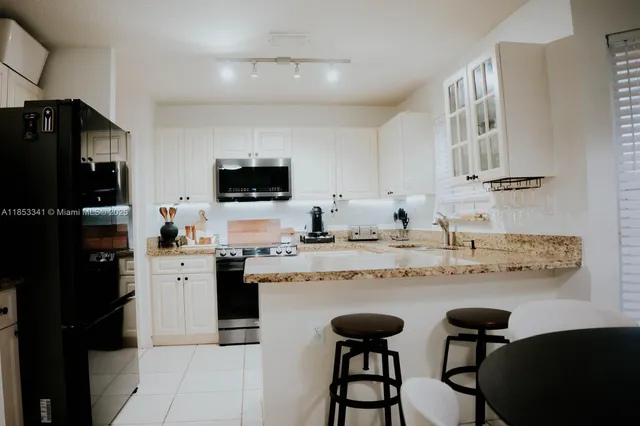 a kitchen with stainless steel appliances granite countertop a stove top oven a sink a refrigerator and white cabinets with wooden floor