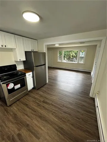 a view of a refrigerator in kitchen and an empty room with wooden floor