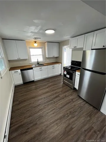 a large kitchen with a refrigerator a sink dishwasher a stove and white cabinets with wooden floor