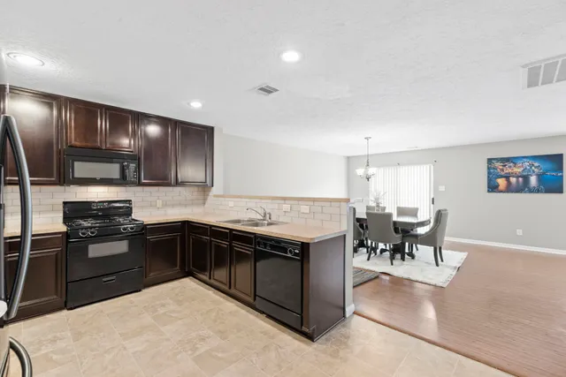 a kitchen with stainless steel appliances granite countertop a stove top oven a sink dishwasher a dining table and chairs with wooden floor