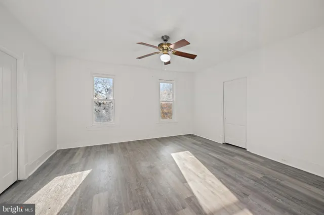 an empty room with wooden floor chandelier fan and windows