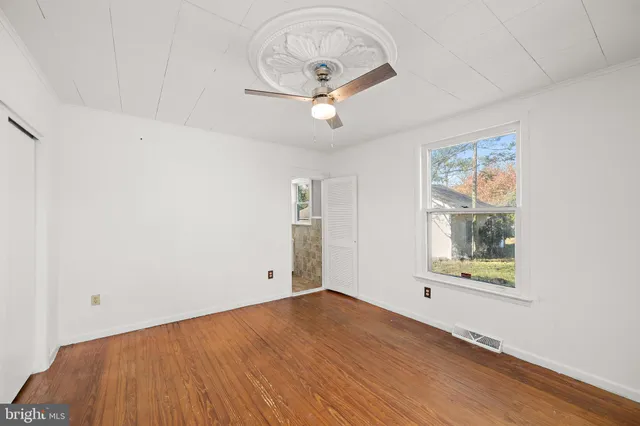 an empty room with wooden floor fan and windows