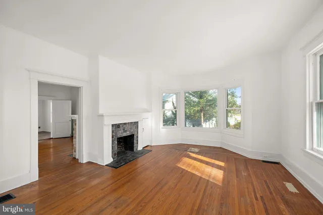 an empty room with wooden floor fireplace and windows