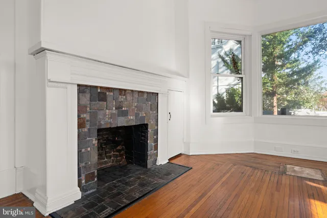 a view of an empty room with wooden floor fireplace and a window