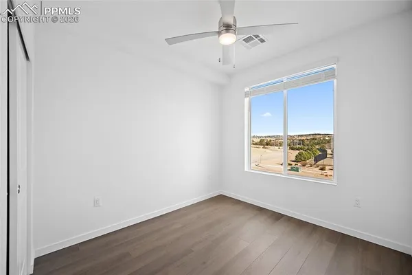 an empty room with wooden floor ceiling fan and windows