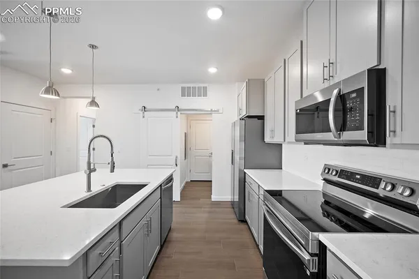 a kitchen with stainless steel appliances kitchen island a white stove top oven a sink dishwasher and a refrigerator with wooden floor
