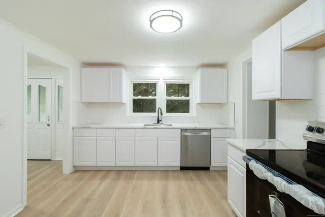 a large white kitchen with granite countertop a sink and a stove top oven