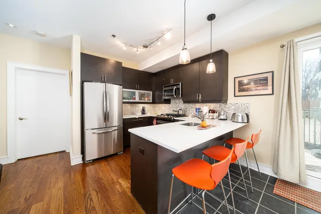 a kitchen with stainless steel appliances a stove a sink a refrigerator a dining table and chairs with wooden floor