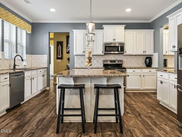 a kitchen with stainless steel appliances granite countertop a stove a sink a microwave a refrigerator white cabinets and chairs