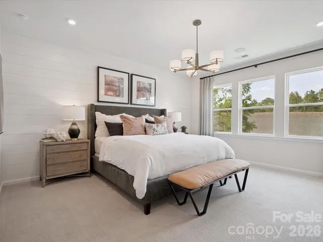 a spacious bedroom with a bed a window and potted plant on the dresser