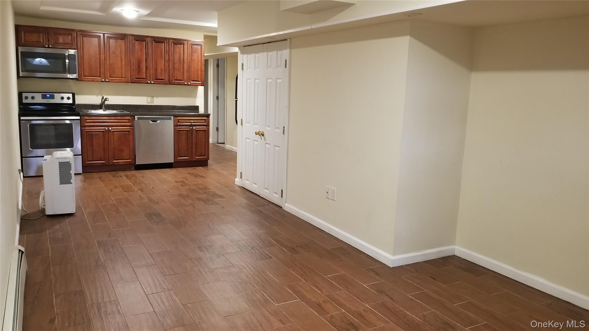 Kitchen with appliances with stainless steel finishes, wood tiled floors, a baseboard radiator, and brown cabinets