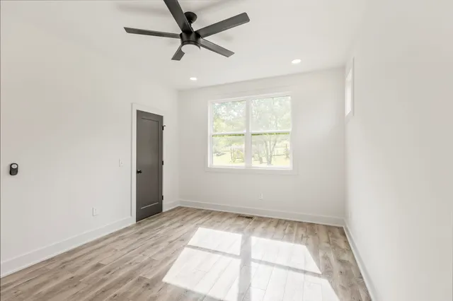 an empty room with wooden floor ceiling fan and windows