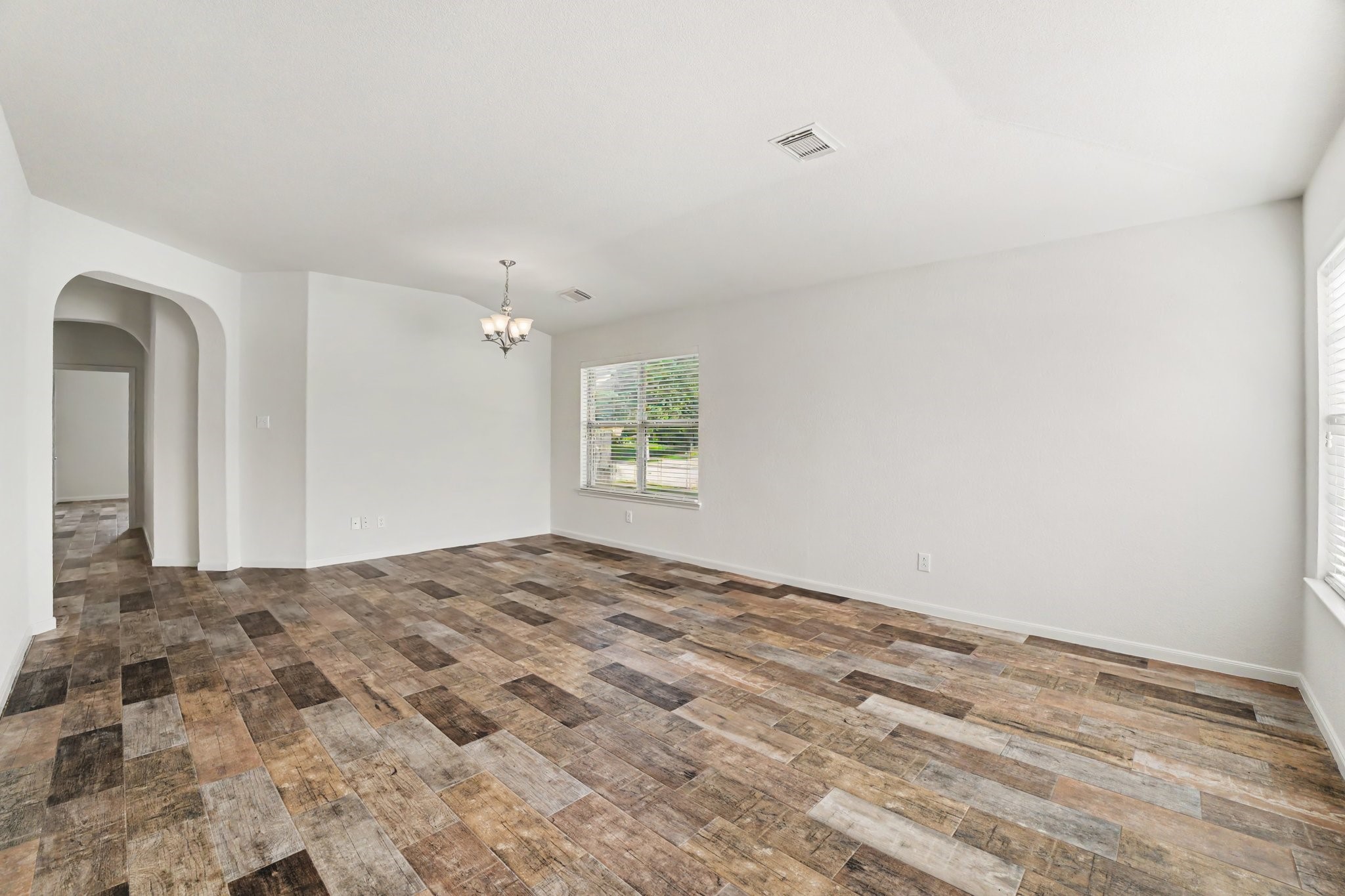 21427 Blooming Rock Lane Spring, TX 77379 - Photo 6 of 32 Bright and spacious living area with stylish wood-look flooring, neutral walls, and ample natural light from large windows. Features a modern light fixture and an open layout that leads into an adjacent hallway through an arched entryway. Ideal for comfortable living and entertaining.