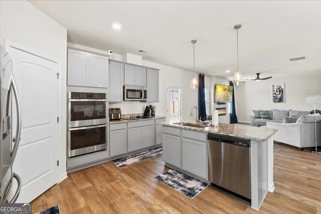 a kitchen with stainless steel appliances granite countertop a stove top oven a sink dishwasher a refrigerator and white cabinets with wooden floor