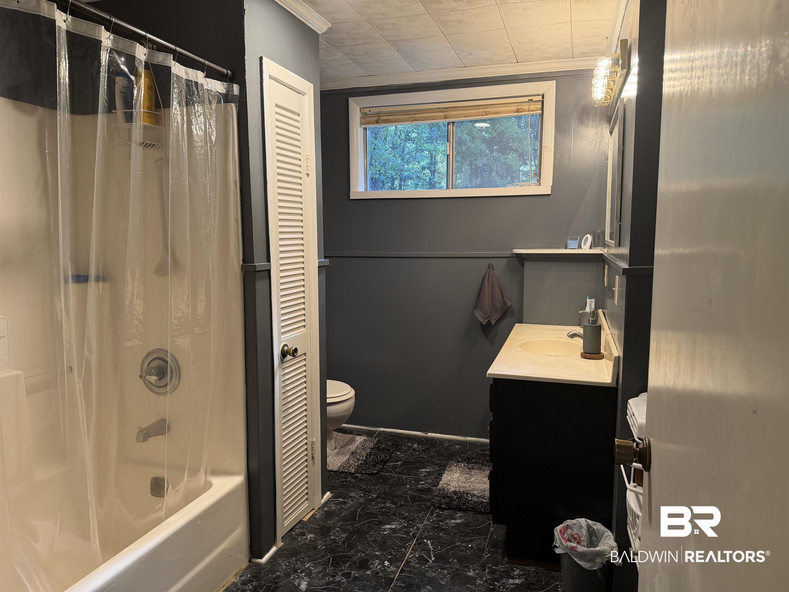 1401 East Forest Ridge Road Mobile, AL 36618 - Photo 10 of 19 Bathroom featuring a white tub-shower combination, a louvered bi-fold door, a window with a blind, a vanity with a light-colored countertop, and dark-toned flooring