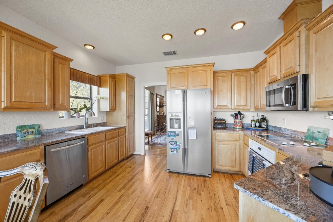 515 Coventry Road Spicewood, TX 78669 - Photo 15 of 36 a kitchen with stainless steel appliances granite countertop wooden cabinets a refrigerator a sink a stove a microwave and wooden floors