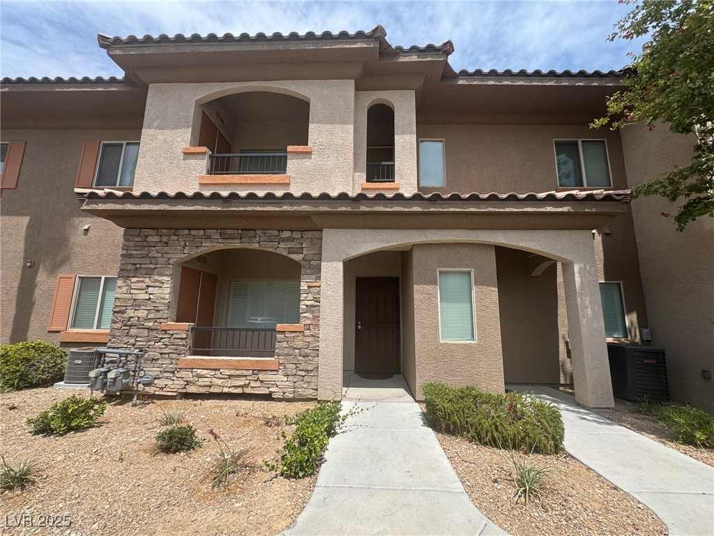 View of front of home with stucco siding, stone siding, a balcony, and a tiled roof