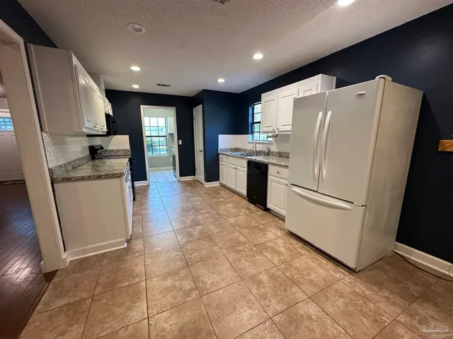 a kitchen with granite countertop a refrigerator a sink and white cabinets