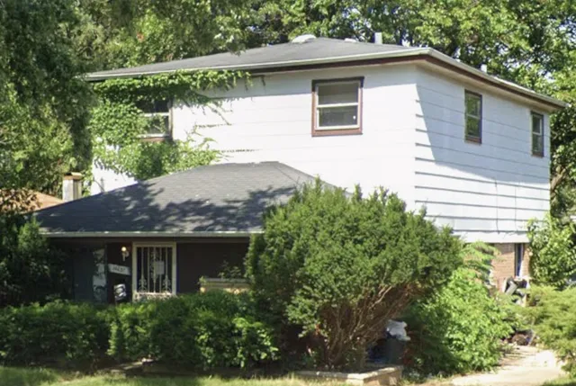 a view of a house with a yard plants and large tree