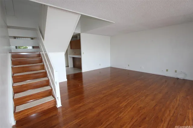 a view of an empty room with wooden floor and stairs