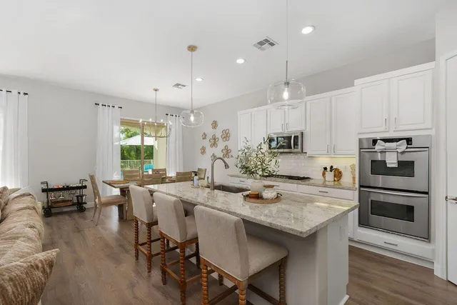 a kitchen with stainless steel appliances granite countertop a stove a refrigerator a kitchen island a dining table and chairs with wooden floor