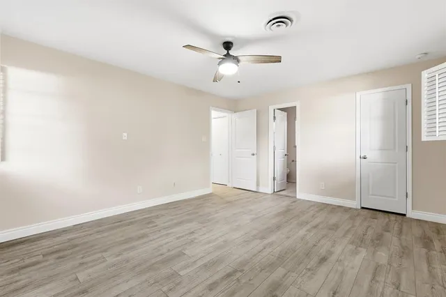 an empty room with wooden floor ceiling fan and windows