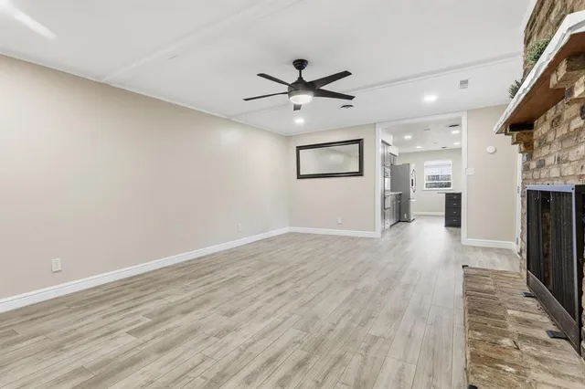 an empty room with wooden floor a ceiling fan a kitchen view and a fireplace