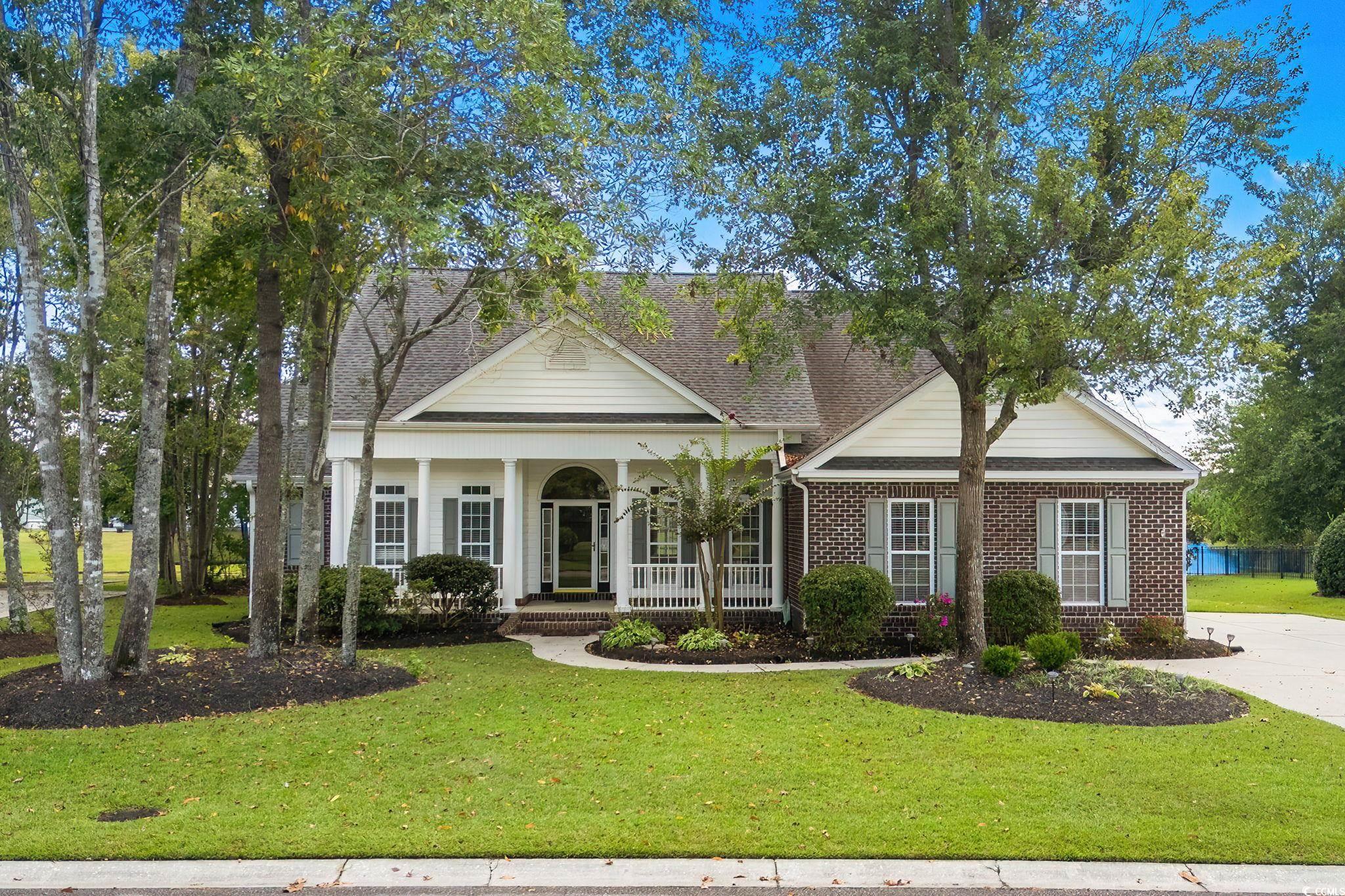 Greek revival house featuring a porch, brick siding, a front lawn, and roof with shingles