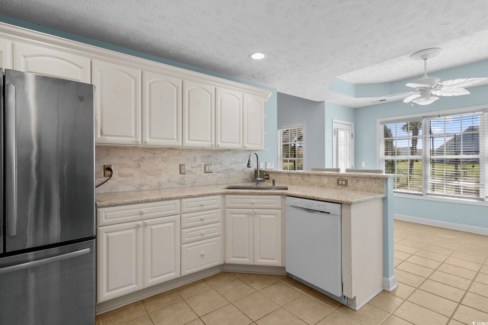613 Broad River Road Myrtle Beach, SC 29588 - Photo 17 of 40 Kitchen featuring freestanding refrigerator, backsplash, light tile patterned floors, a peninsula, and white dishwasher