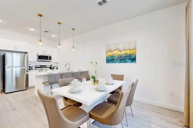 a dining room with stainless steel appliances kitchen island granite countertop a dining table chairs and a refrigerator