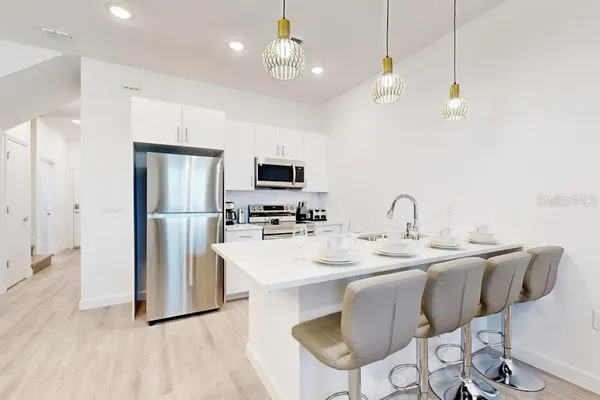 a kitchen with stainless steel appliances kitchen island granite countertop a sink a refrigerator and a dining table with wooden floor