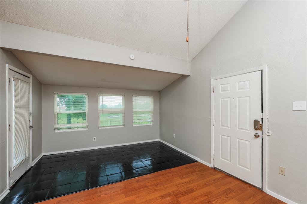 9696 Walnut Street, Unit 1216 Dallas, TX 75243 - Photo 11 of 16 Vaulted ceiling room featuring a combination of wood-finish flooring and black tile, multiple windows with blinds, and a white panel door