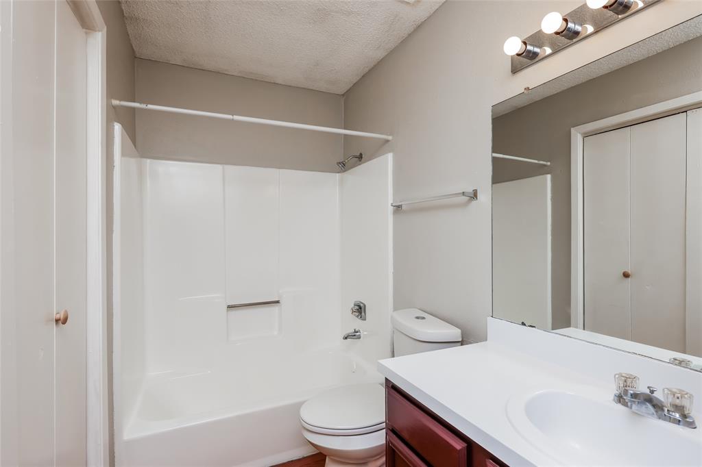 9696 Walnut Street, Unit 1216 Dallas, TX 75243 - Photo 13 of 16 Bathroom featuring a white tub/shower combination, a vanity with a white countertop and wood-finish cabinetry, a toilet, a wall-mounted mirror, and a three-bulb light fixture