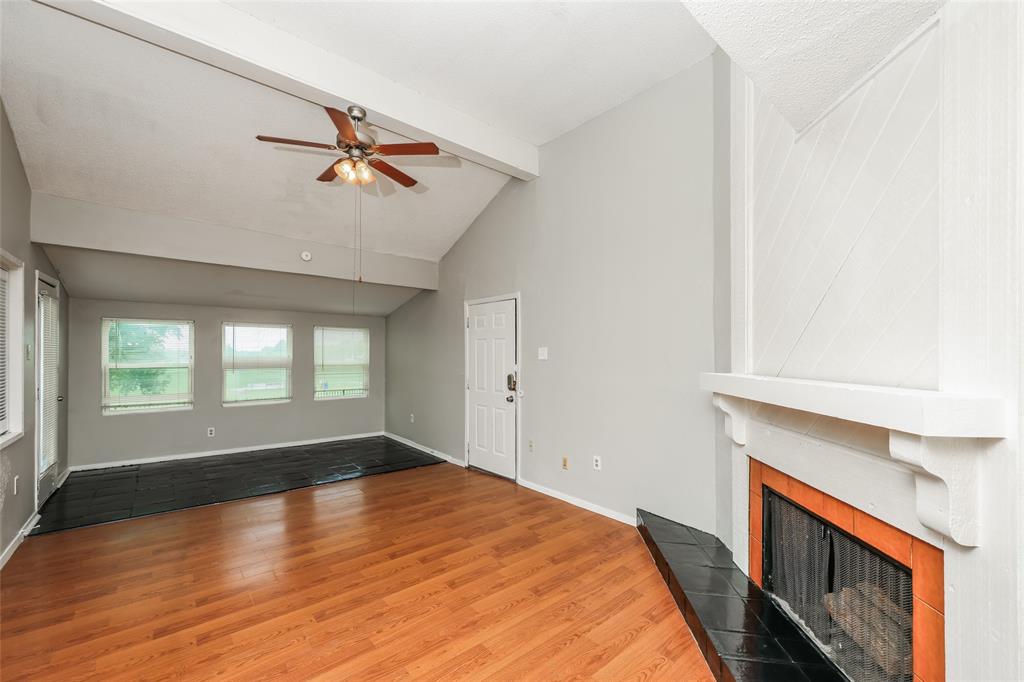 9696 Walnut Street, Unit 1216 Dallas, TX 75243 - Photo 3 of 16 Spacious living area featuring wood-finish flooring, a vaulted ceiling with a ceiling fan, a fireplace with a white mantel and black tile hearth, and multiple windows