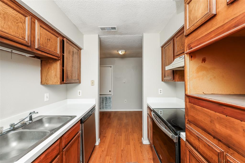 9696 Walnut Street, Unit 1216 Dallas, TX 75243 - Photo 7 of 16 Galley kitchen featuring wood-finish cabinetry, white countertops, a double basin stainless steel sink, and wood-finish flooring